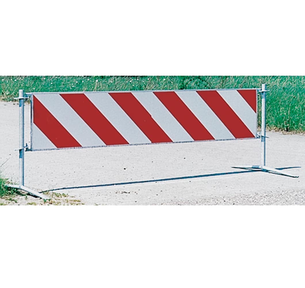 Portable barrier with red diagonal stripes blocking a dirt road construction site access point