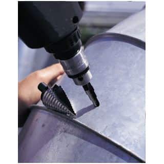 Close-up of a hand operating a power drill to make a hole in a galvanized metal cylindrical surface (a duct).