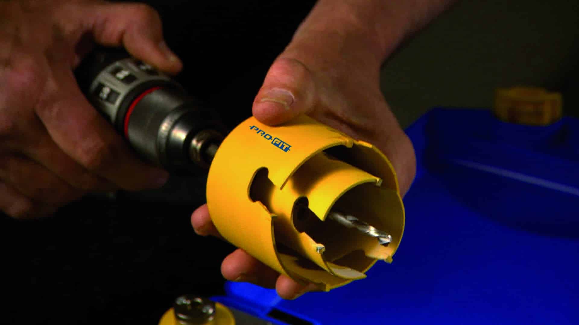Close-up of hands using a drill to assemble a yellow plastic pipe coupling in a workshop setting