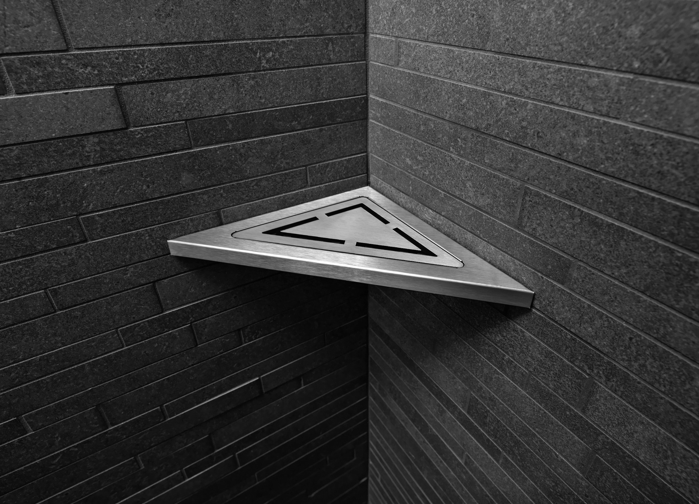 Corner where two dark brick walls meet, with a stainless steel triangular platform featuring a cut-out triangle pattern.