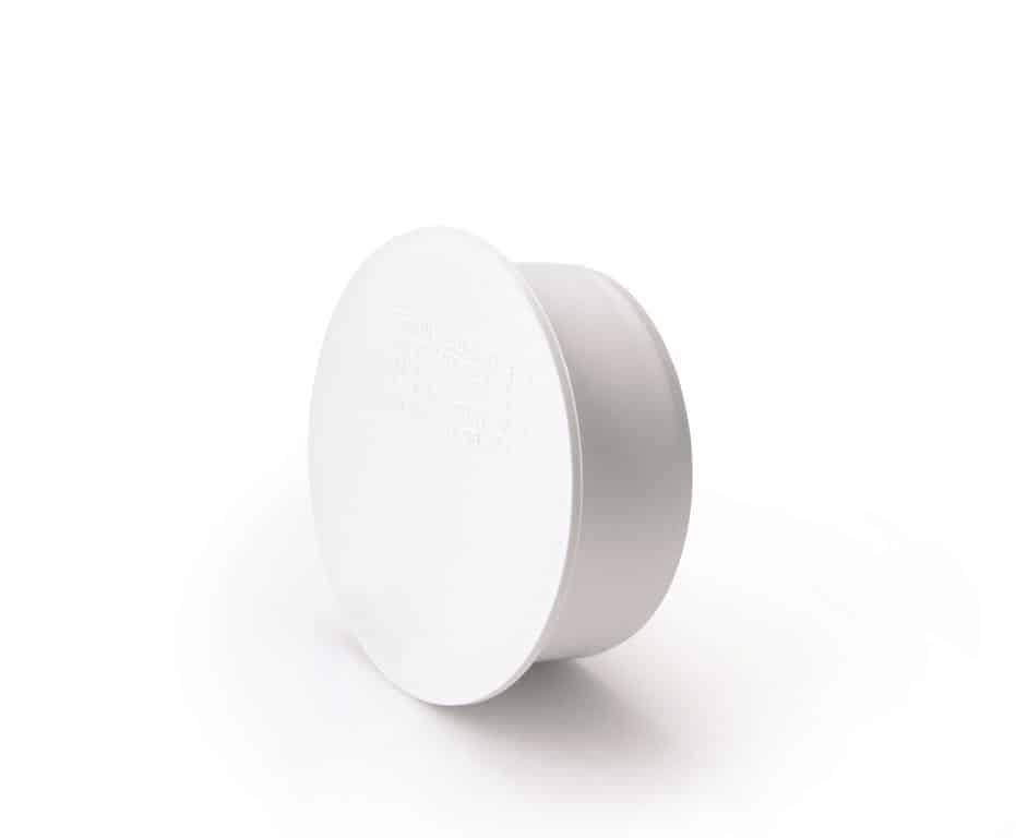 White plastic circular lid seen at an angle on a white surface.