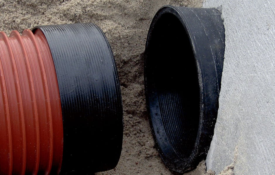 Red corrugated flexible drainage pipe next to a black PVC fitting entering a concrete wall cavity
