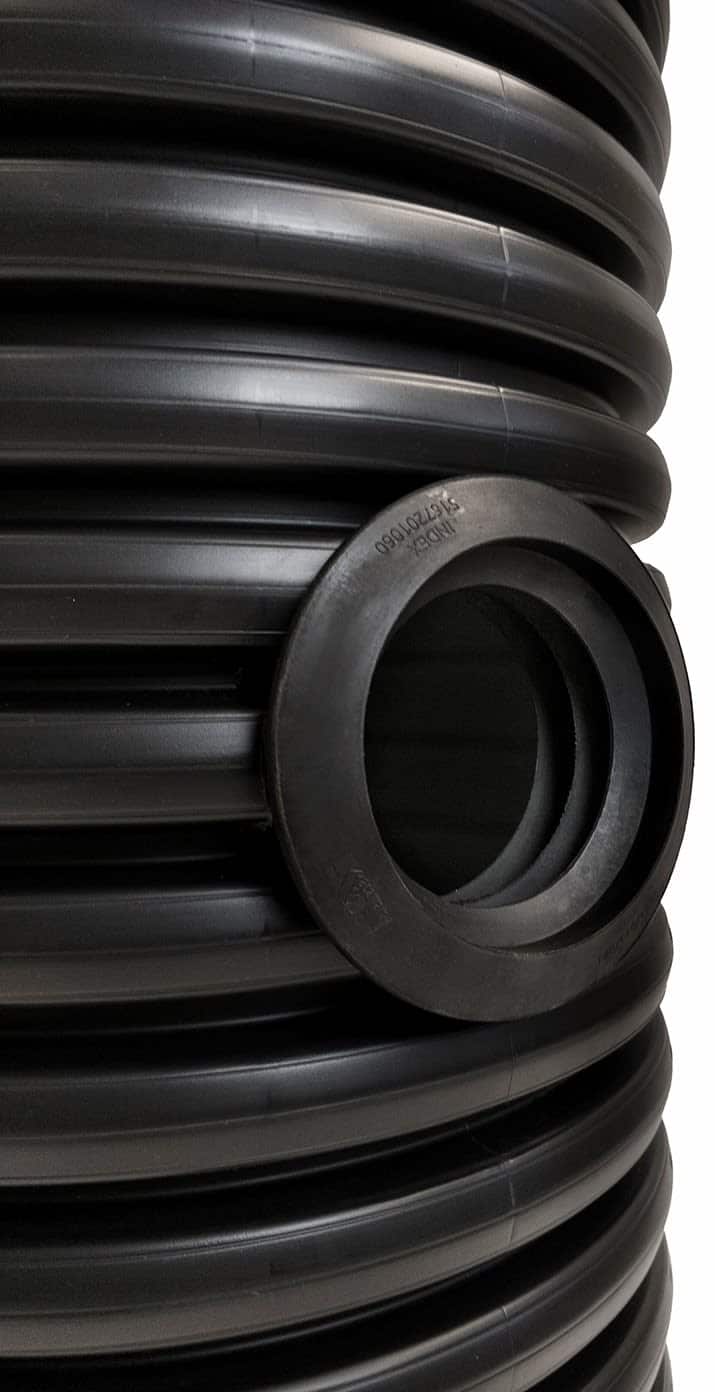Coiled black corrugated plastic pipe with a round connector fitting on the side.