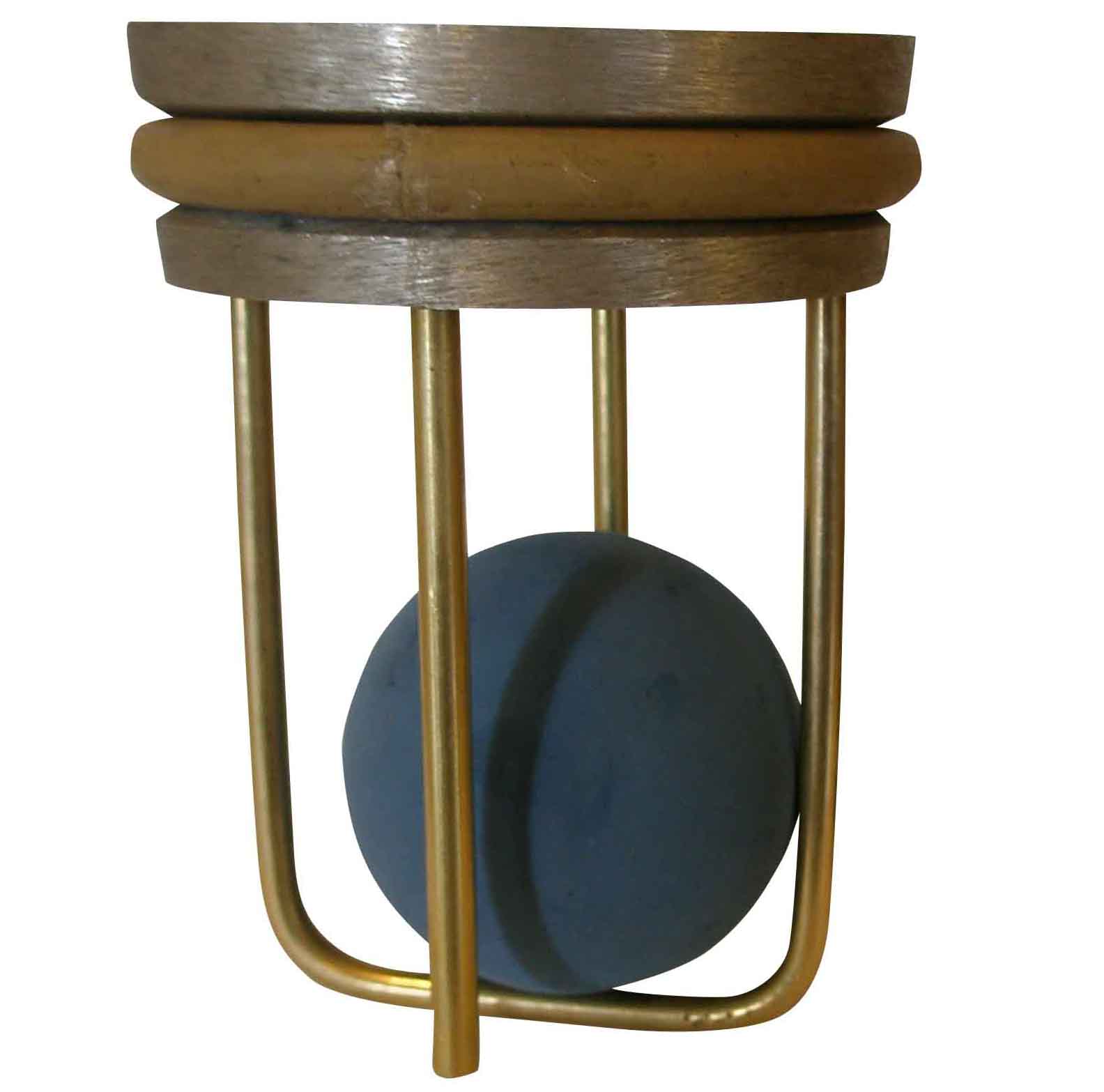 Close-up of a modern sculpture: three stacked circular wooden disks supported by gold rods around a blue circular core.