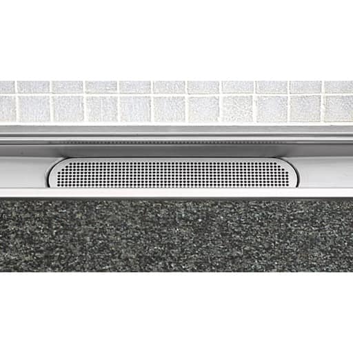 Perforated metal vent strip at the base of a doorway between a tiled wall and concrete floor.