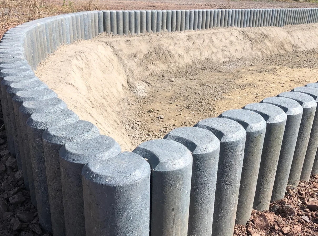 Curved row of gray concrete bollards forming a barrier around a dirt excavation at a construction site.