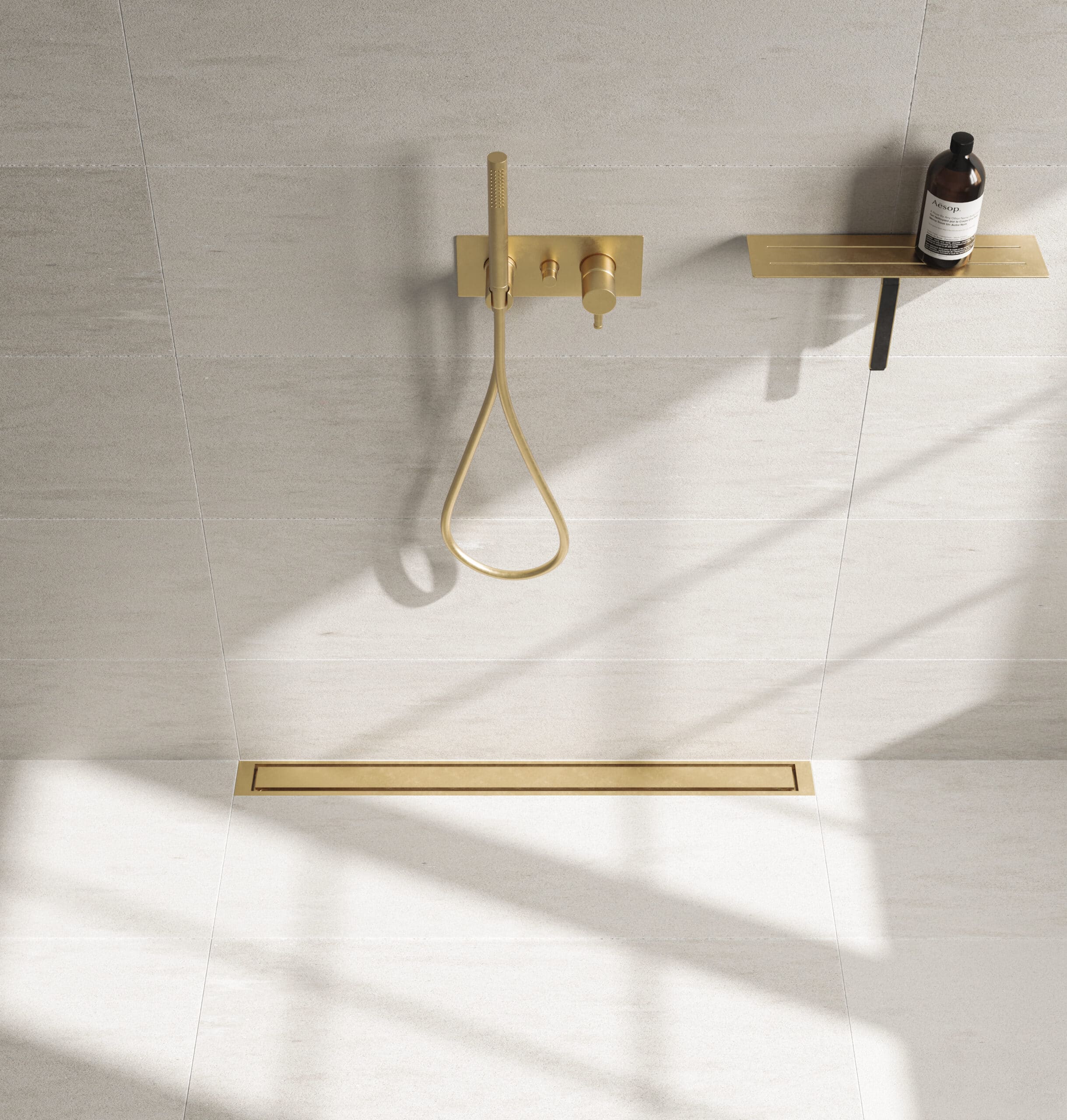 Gold bathroom shower fixture with handheld wand mounted on a rectangular plate, plus a slim shelf holding a brown bottle, all against beige tile.