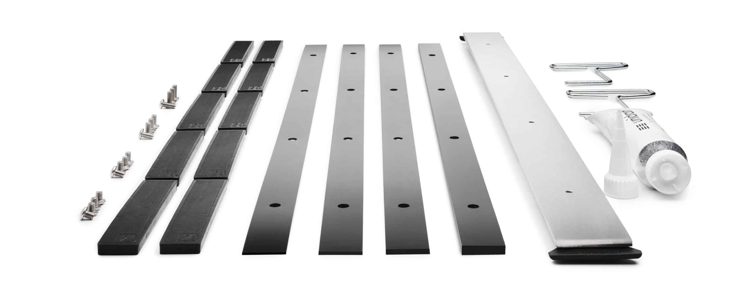 Assorted metal hardware parts arranged in a row: black rails, silver slotted bars, screws, brackets, and a tube of adhesive/tooling kit for furniture assembly