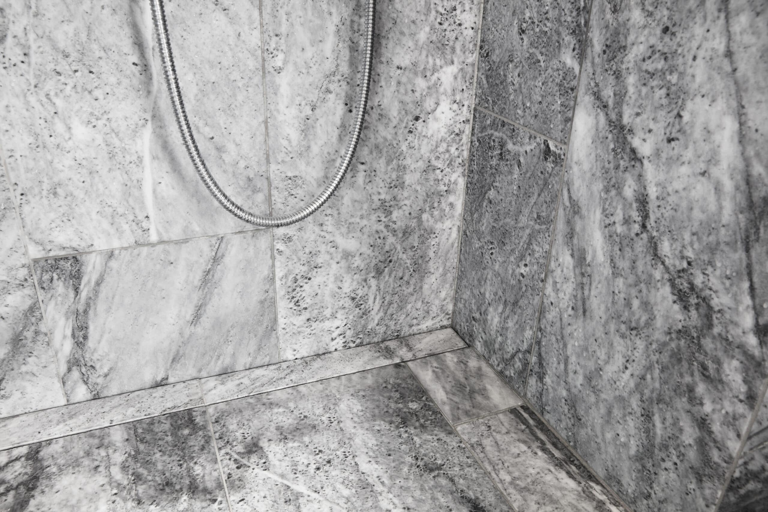 Gray marble-tiled shower wall with a curved chrome flexible shower hose hanging down