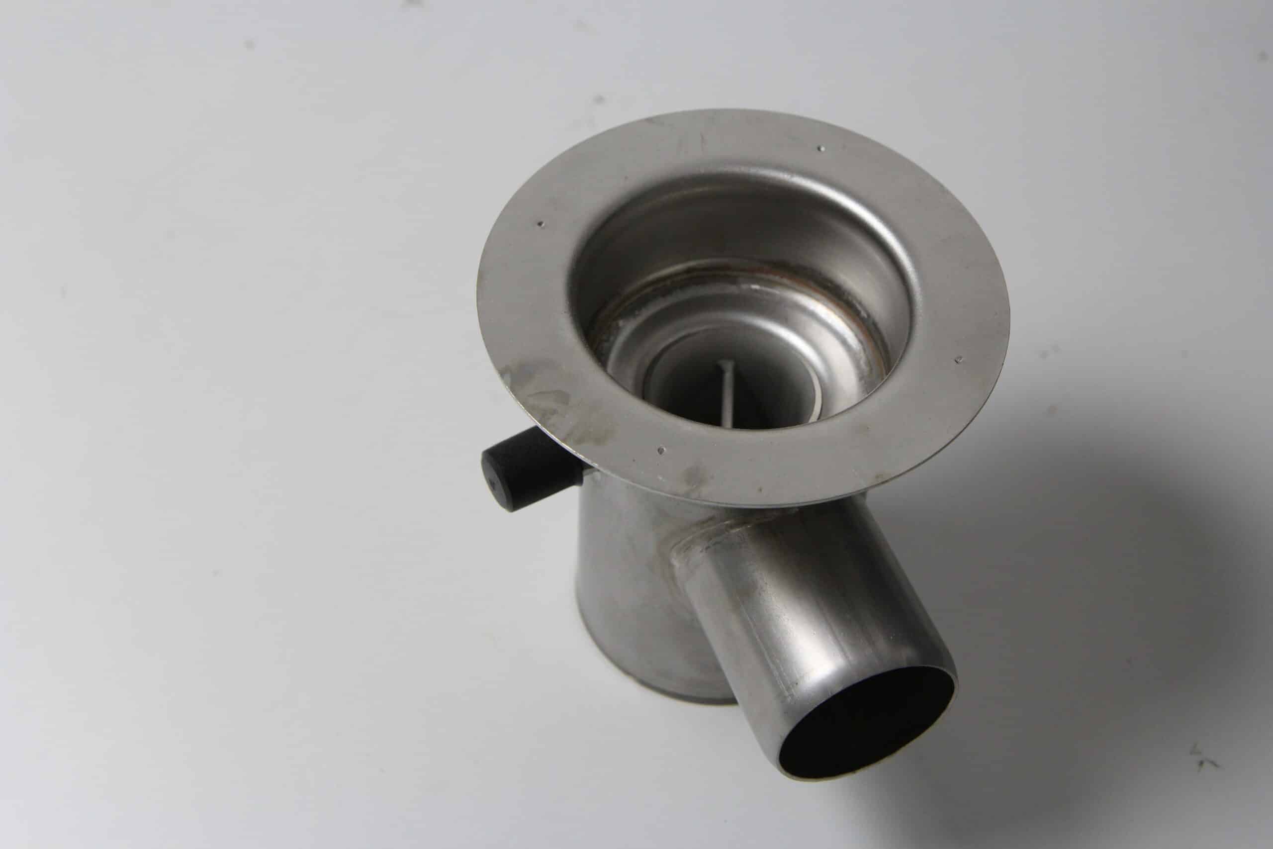 Close-up of a metal pipe fitting with a circular flange and angled tubes, metallic gray finish.
