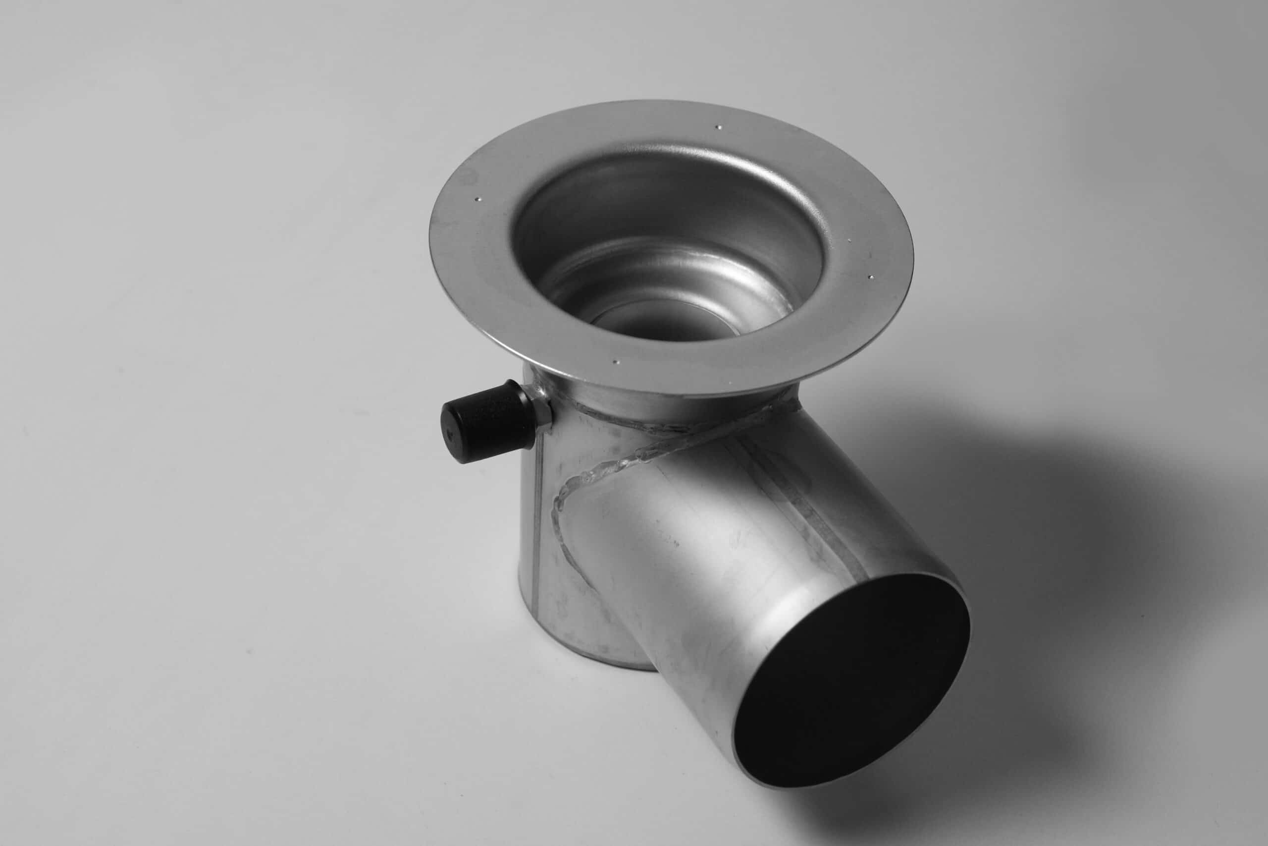 Close-up of a metal duct elbow with a circular flange and open ends, used in ventilation piping.
