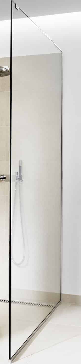 Frameless glass shower enclosure with a handheld showerhead mounted on beige tiled walls and a linear drain along the light tiled floor.