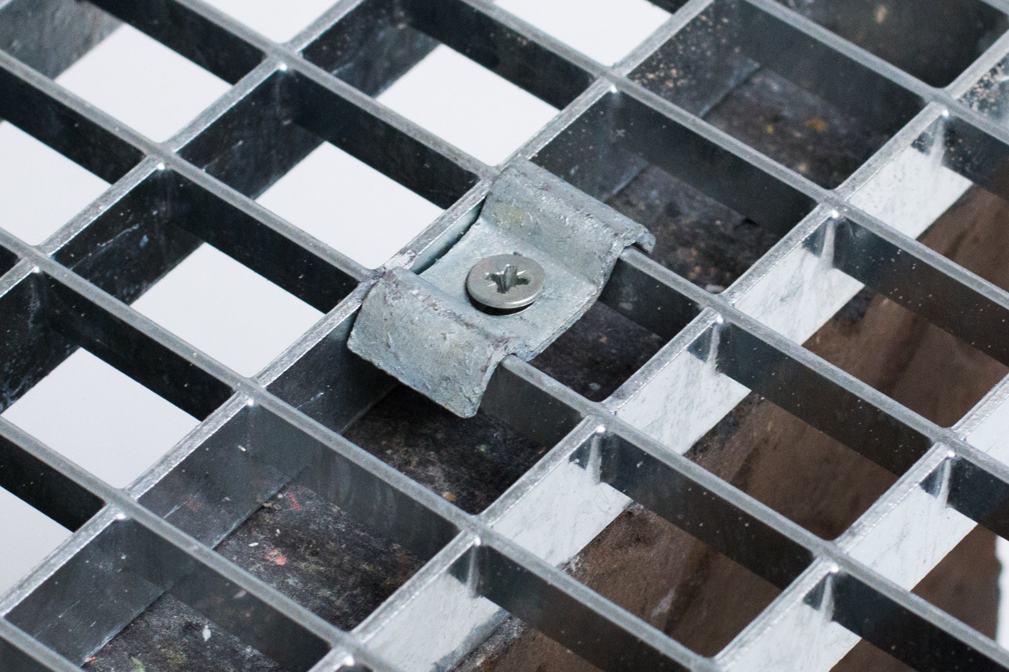Close-up of a metal grate with square openings and a rusted bracket and screw.