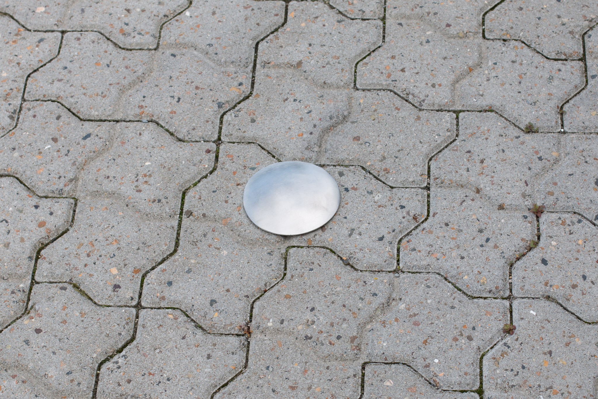 Round metal cover resting on a gray interlocking-paver sidewalk surface